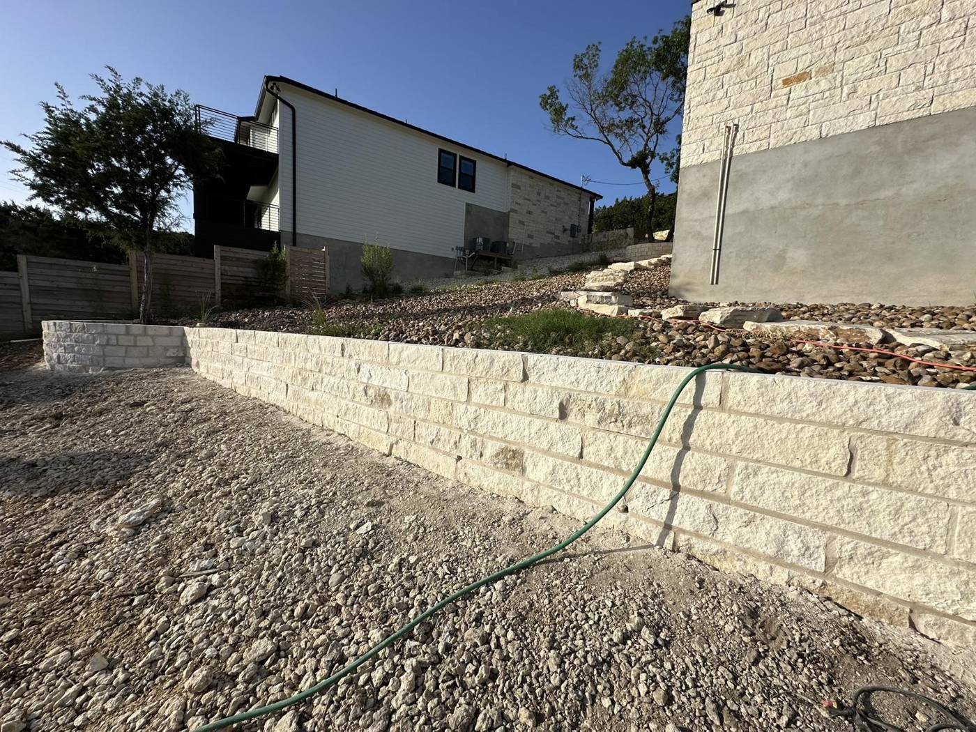 Chopped limestone block retaining wall holding a slope beside a modern Hill Country home