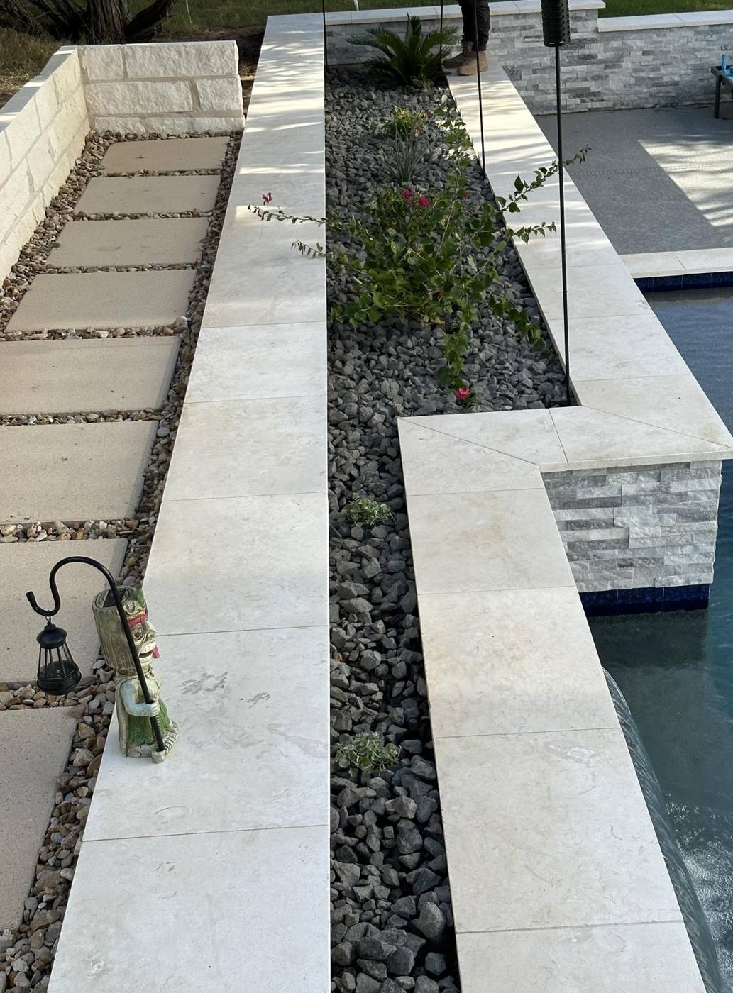 Limestone coping and river rock planter beside a pool with stacked-stone accent wall