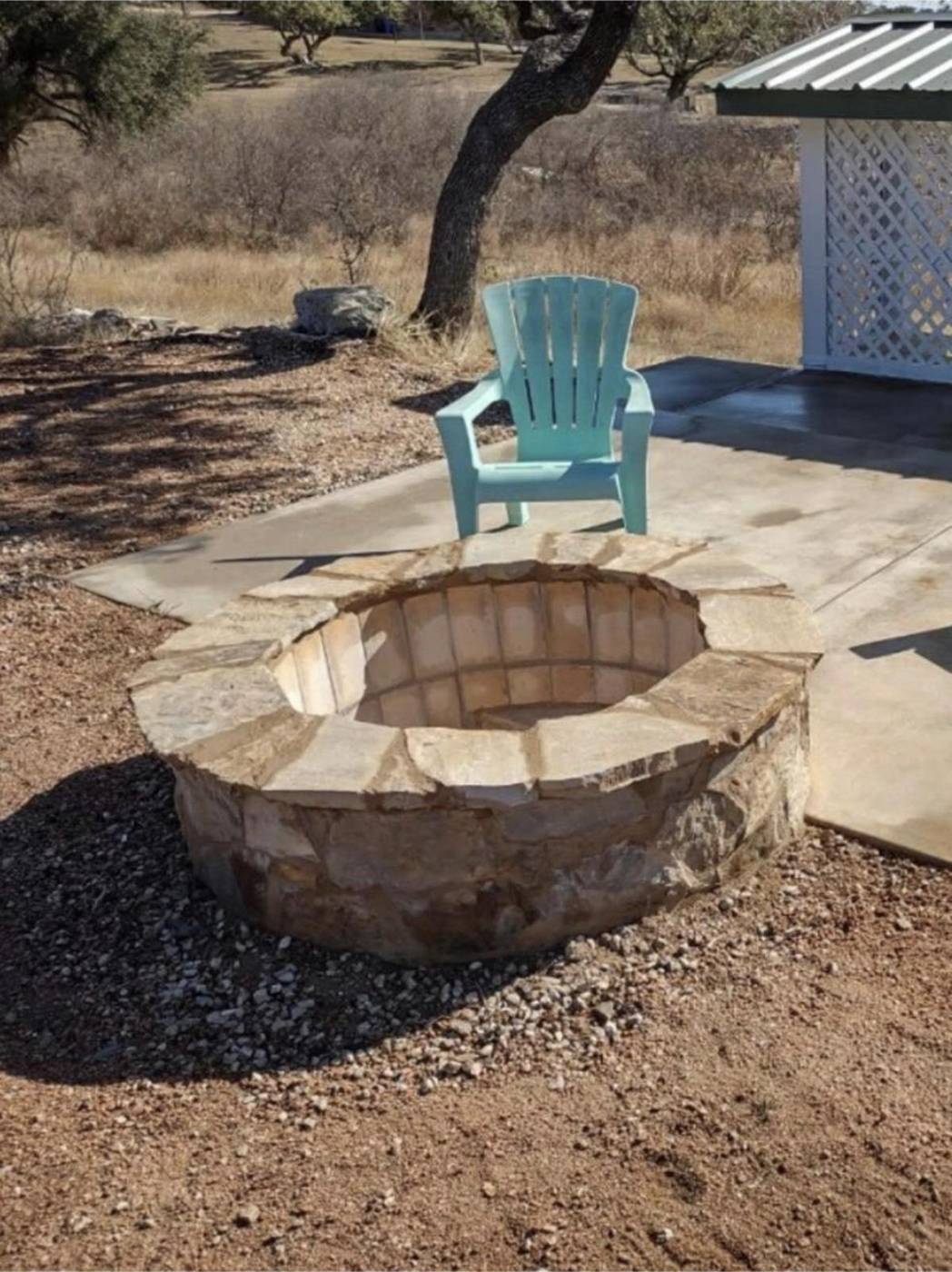 Chopped limestone fire pit beside a flagstone patio under a Hill Country oak