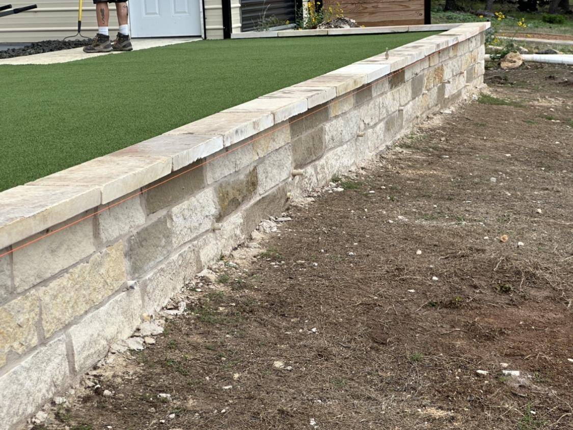 Chopped limestone garden wall edging an artificial turf lawn