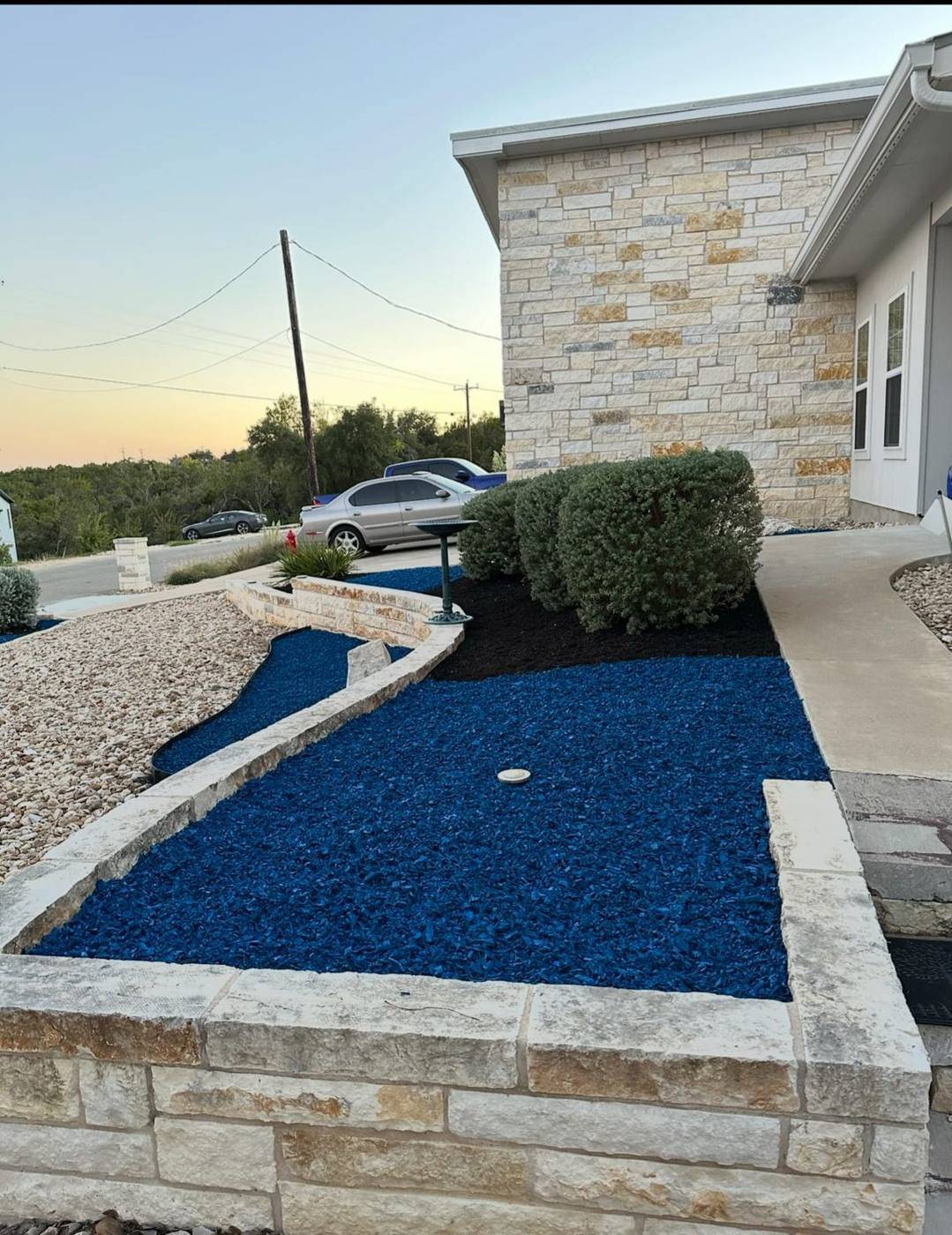 Chopped limestone raised flower bed and low stone wall with blue mulch and decorative rock at a Texas Hill Country home