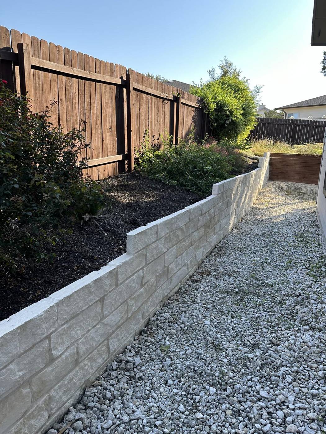 Long limestone raised garden bed along a fence with a crushed gravel path