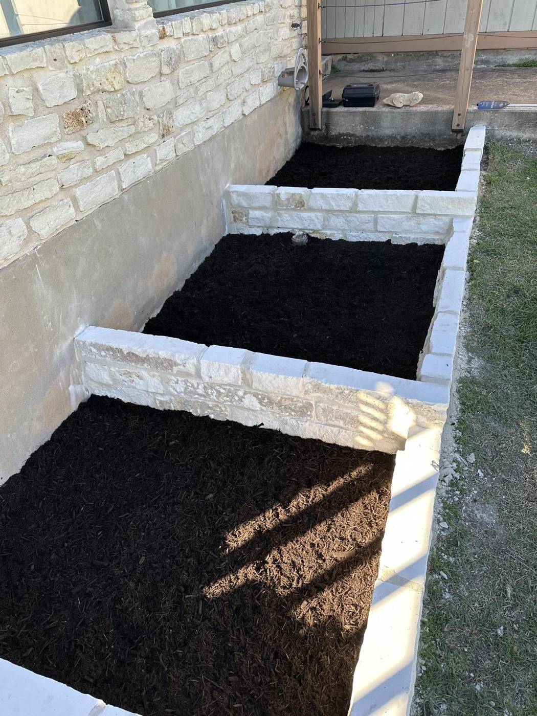 Three chopped limestone raised garden beds filled with fresh soil beside a home
