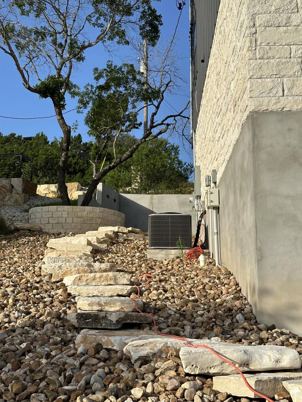 Stacked limestone slab steps with river rock beside a modern Hill Country home