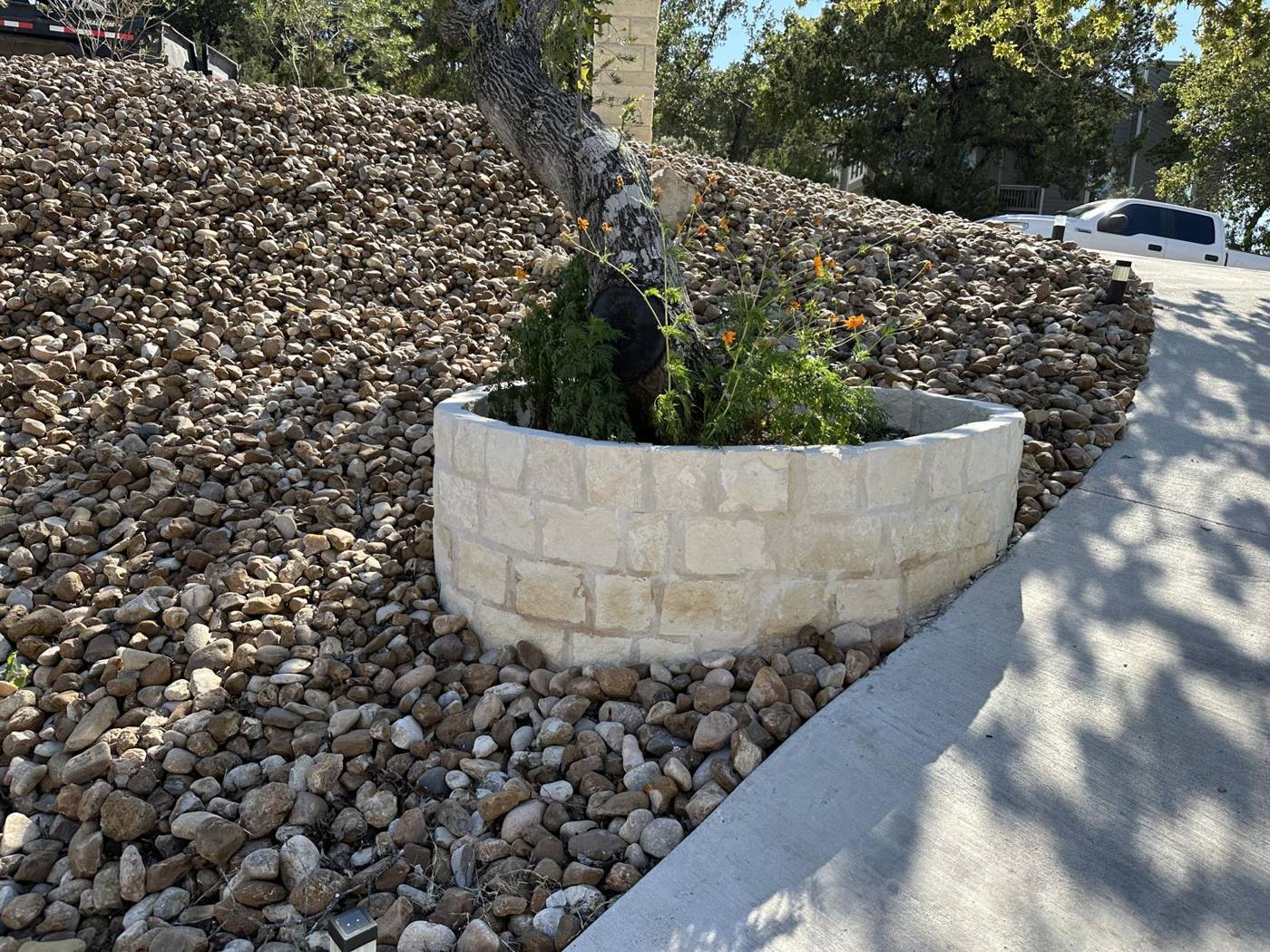 Chopped limestone tree ring with flowers set in river rock landscaping