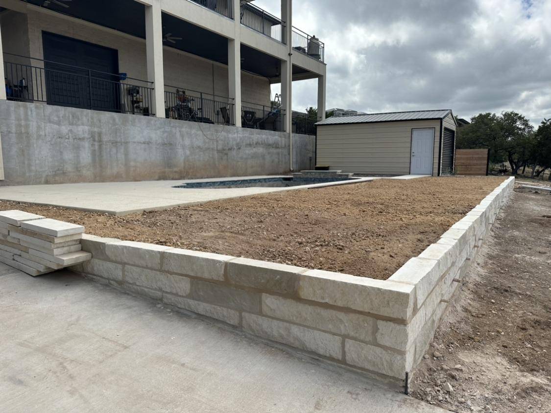 Long limestone raised planter bed filled with soil in front of a modern home