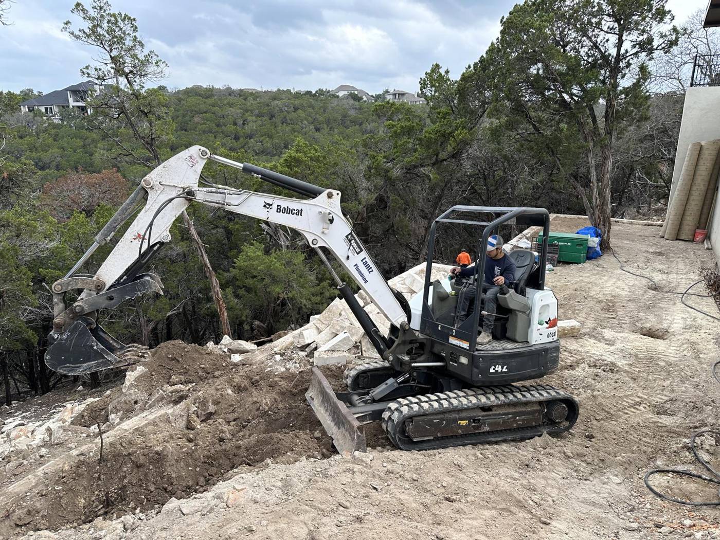 Mini excavator digging and prepping a wooded hillside lot