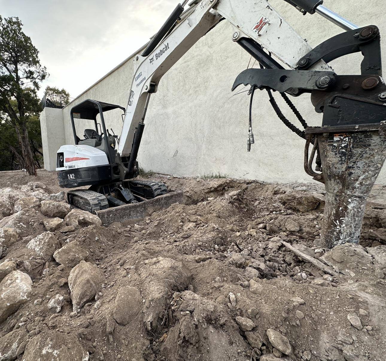 Mini excavator with a hydraulic breaker cutting into limestone rock