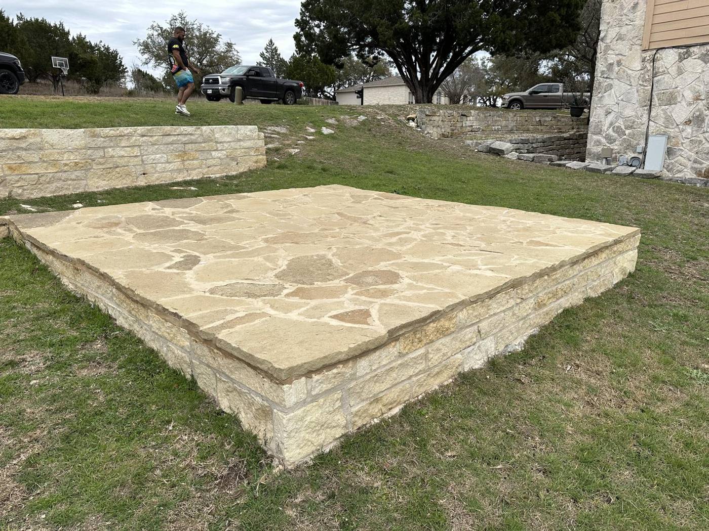 Raised flagstone patio framed by a chopped limestone retaining wall in a Texas back yard