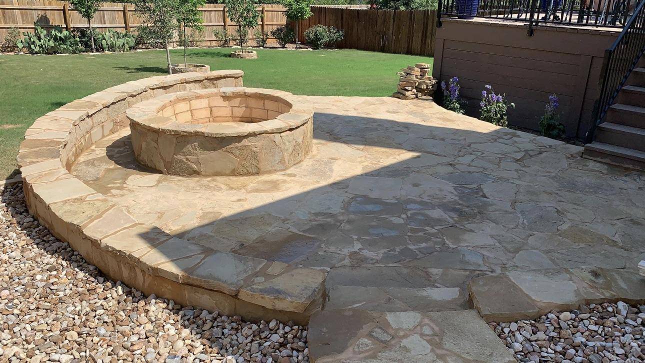 Round limestone fire pit on a flagstone patio with a curved stone seat wall