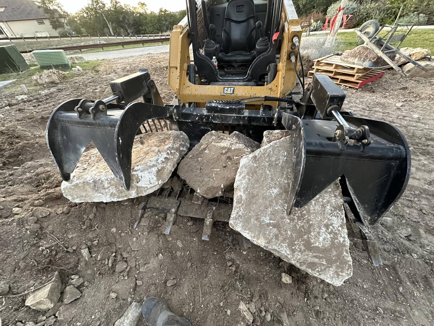 Skid steer grapple bucket moving limestone boulders on a job site