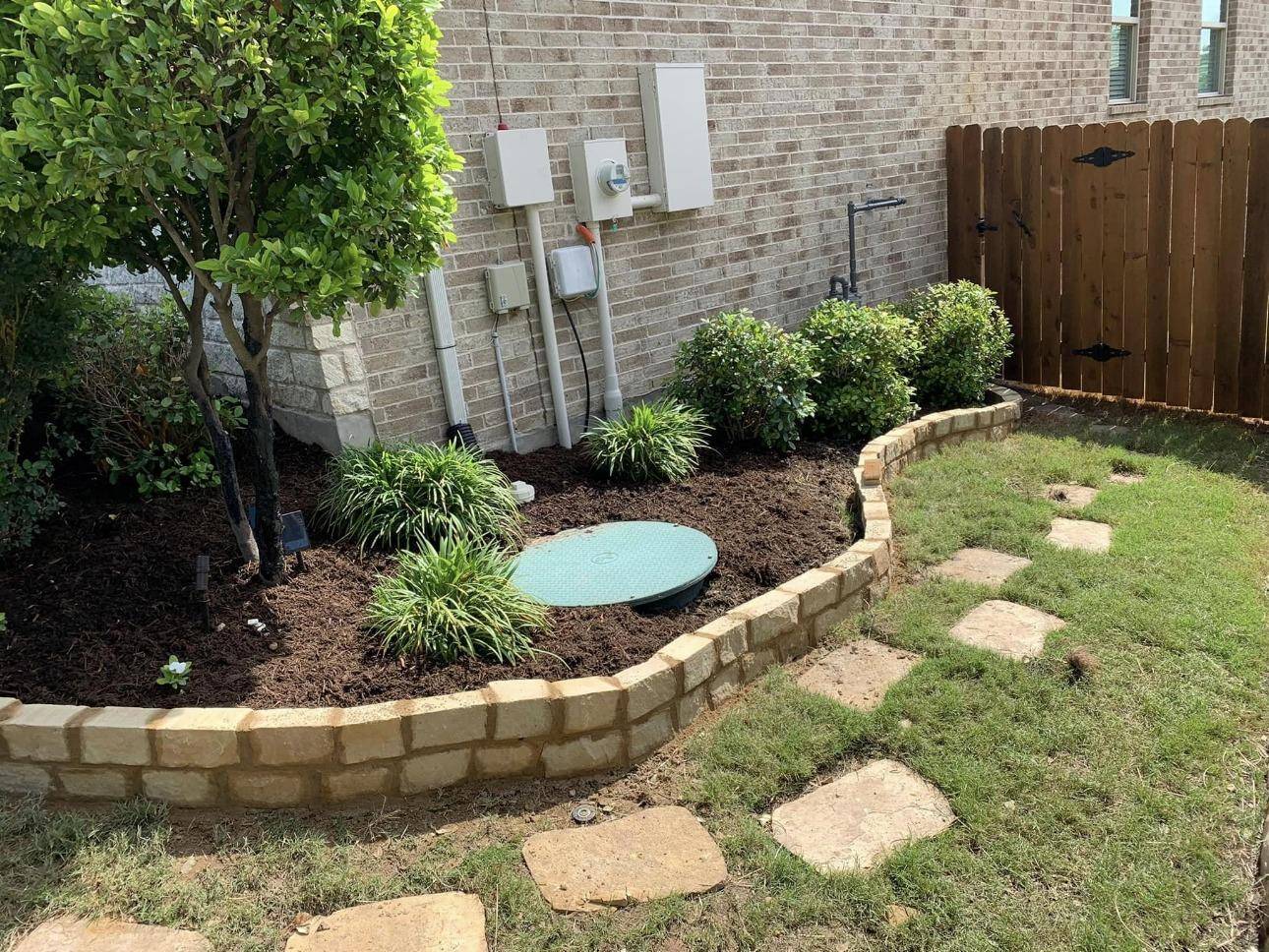 Stone-bordered shrub bed with flagstone stepping stones beside a brick home
