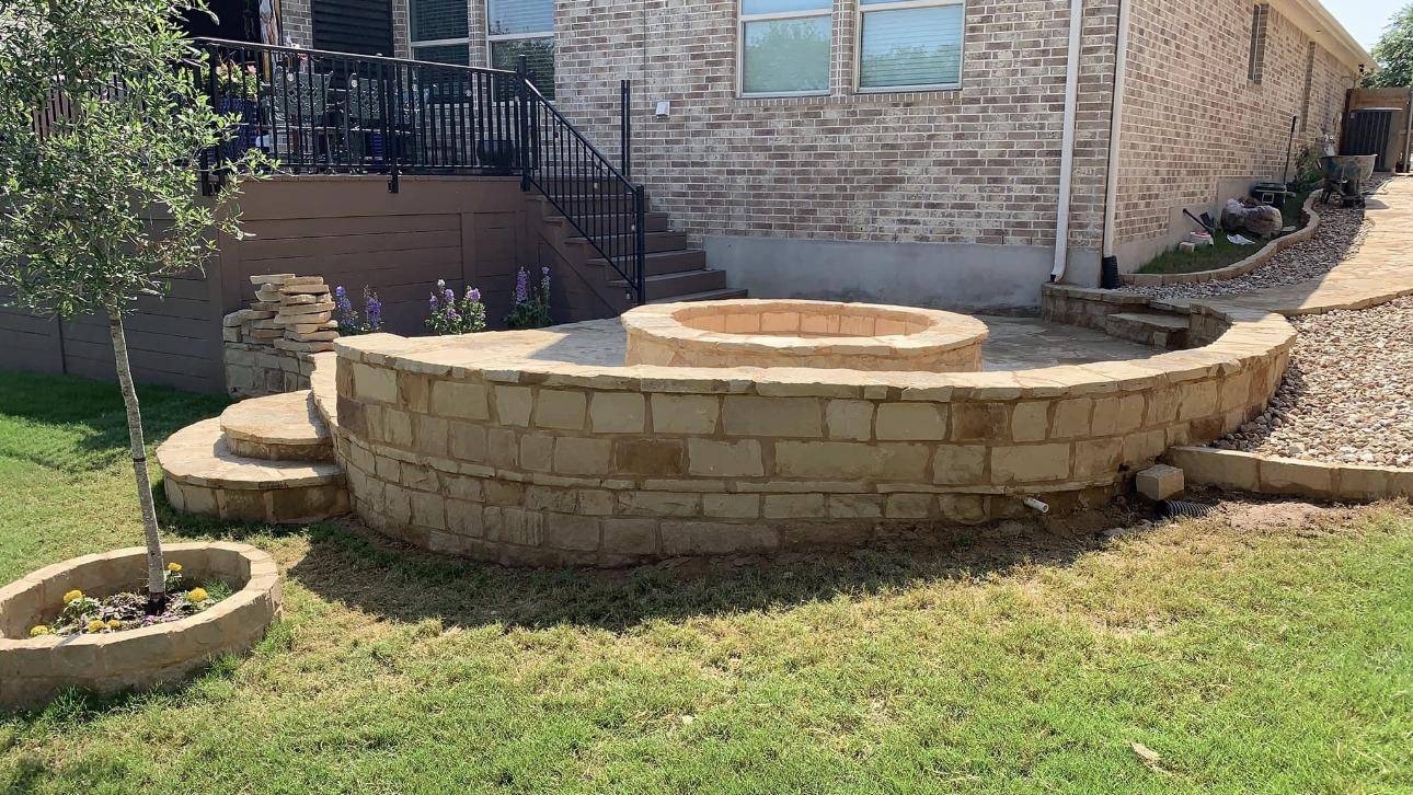 Stone fire pit with curved limestone seat wall and steps in a Texas back yard