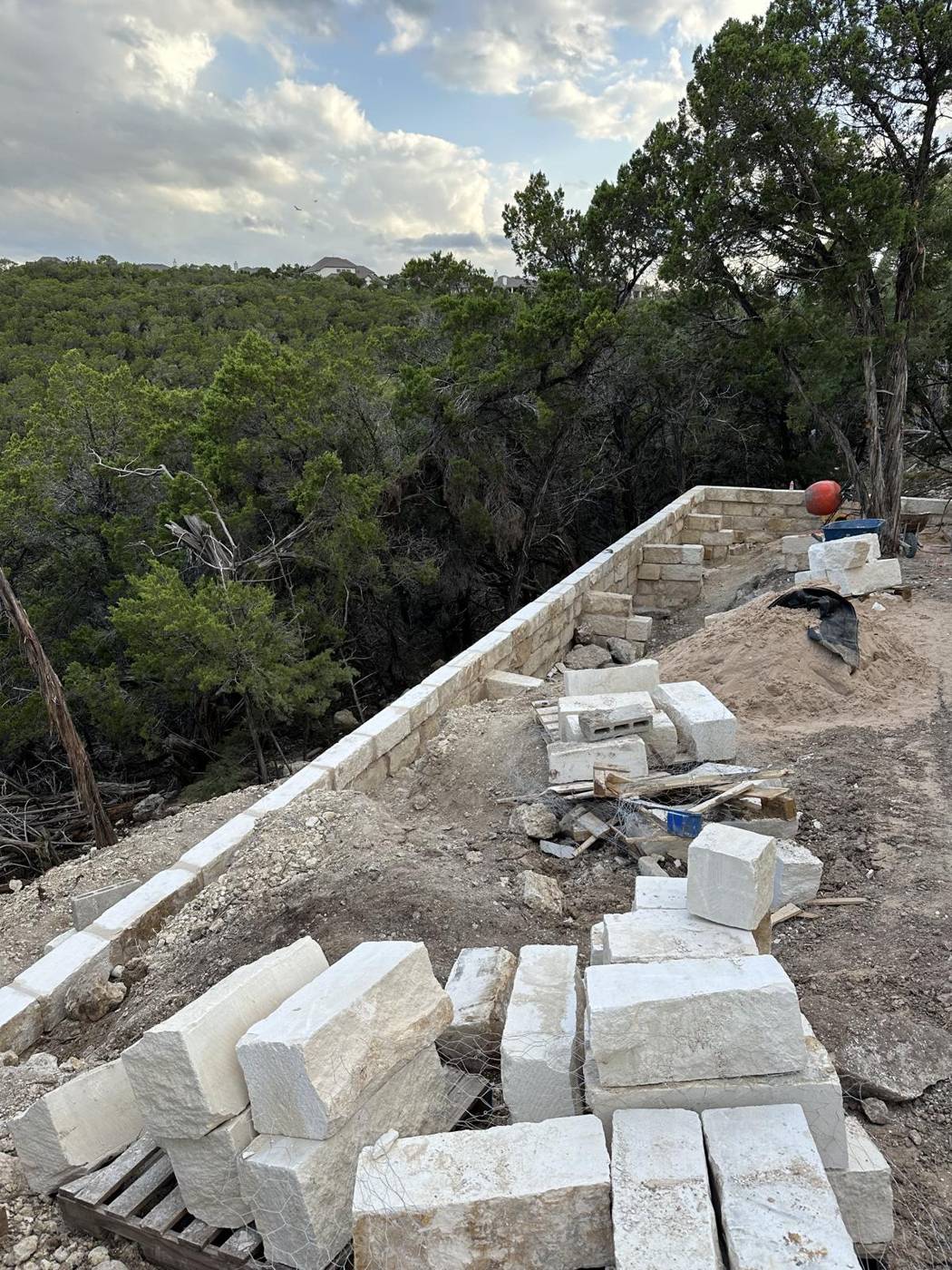 Limestone block retaining wall being built along a steep wooded hillside lot